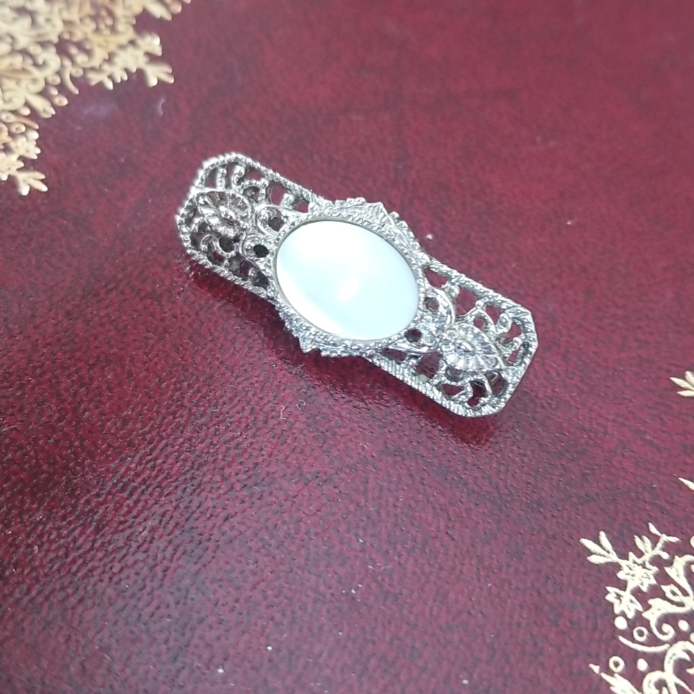 Silver-tone filigree brooch with white glass cat's eye center cabochon. Vintage